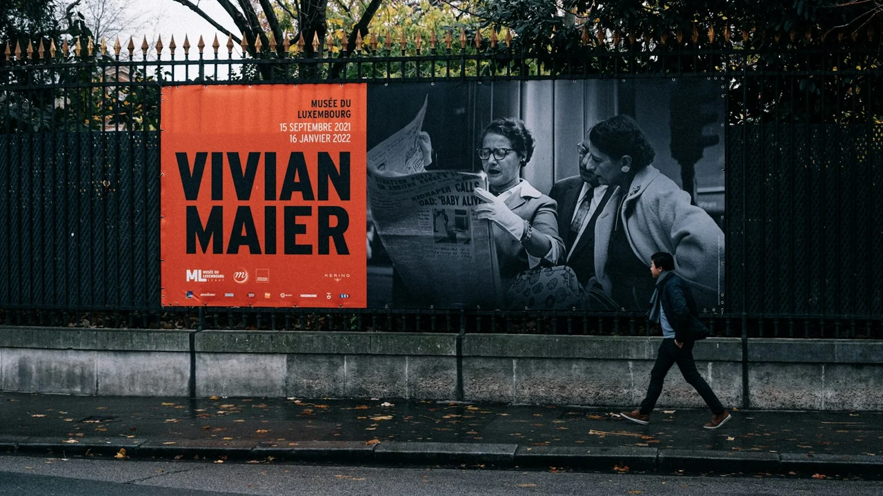 A pedestrian passing a printed exhibition advertisement in Paris
